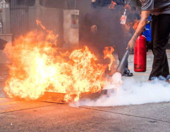 Person using a fire extinguisher to put out a fire during a safety training session.